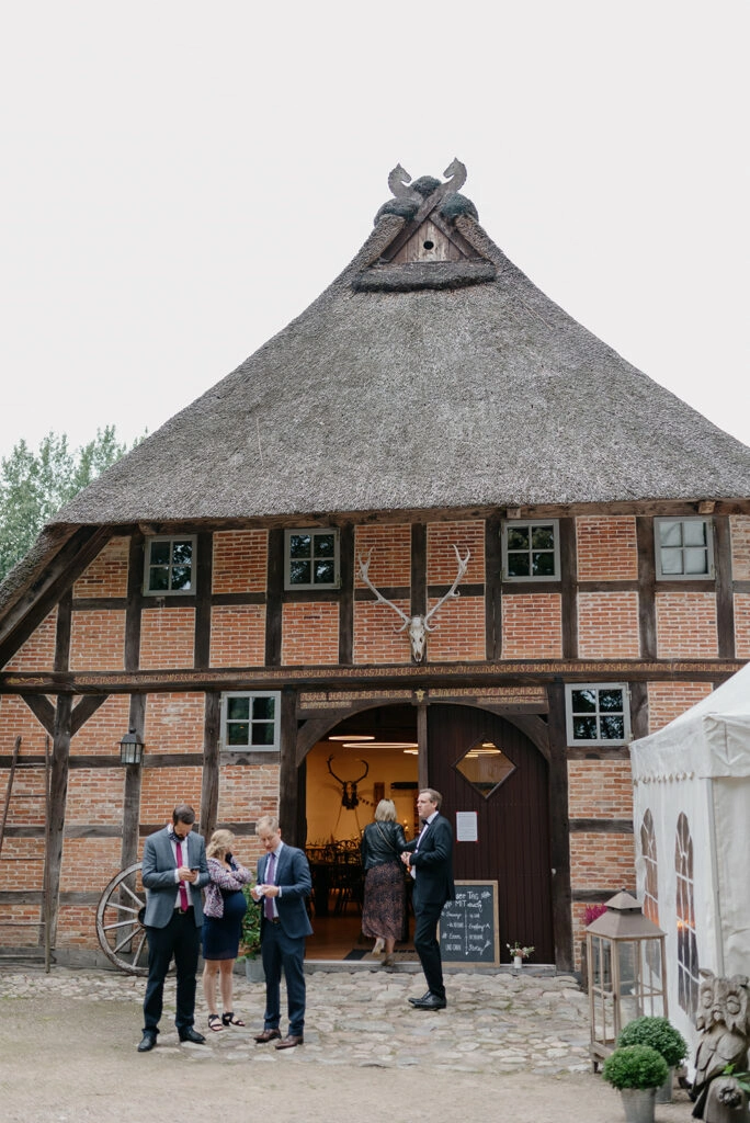 Hochzeitsgäste stehen vor dem großen Tor des Reetdachhauses.