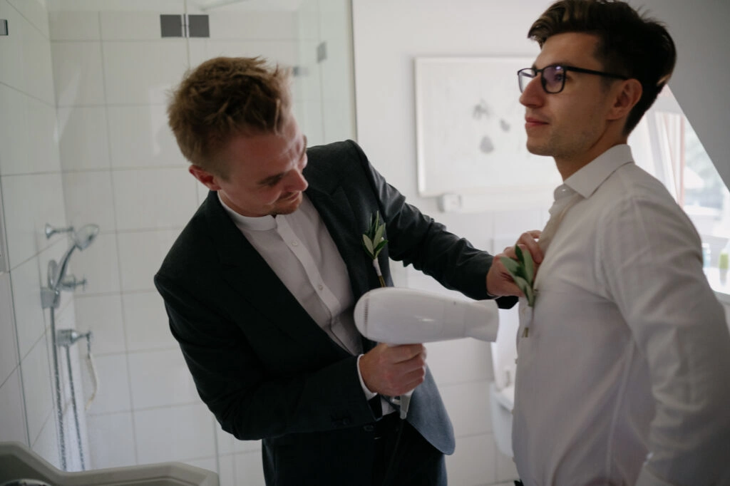Bräutigam hilft einem Begleiter beim Anziehen.