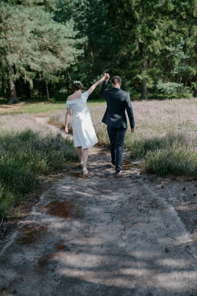 Brautpaar tanzt auf einem Weg durch die Heide.