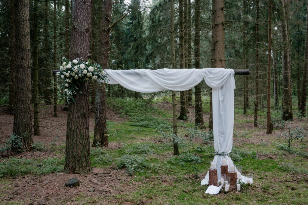 Mit weißem Stoff geschmückter Traubogen im Wald.
