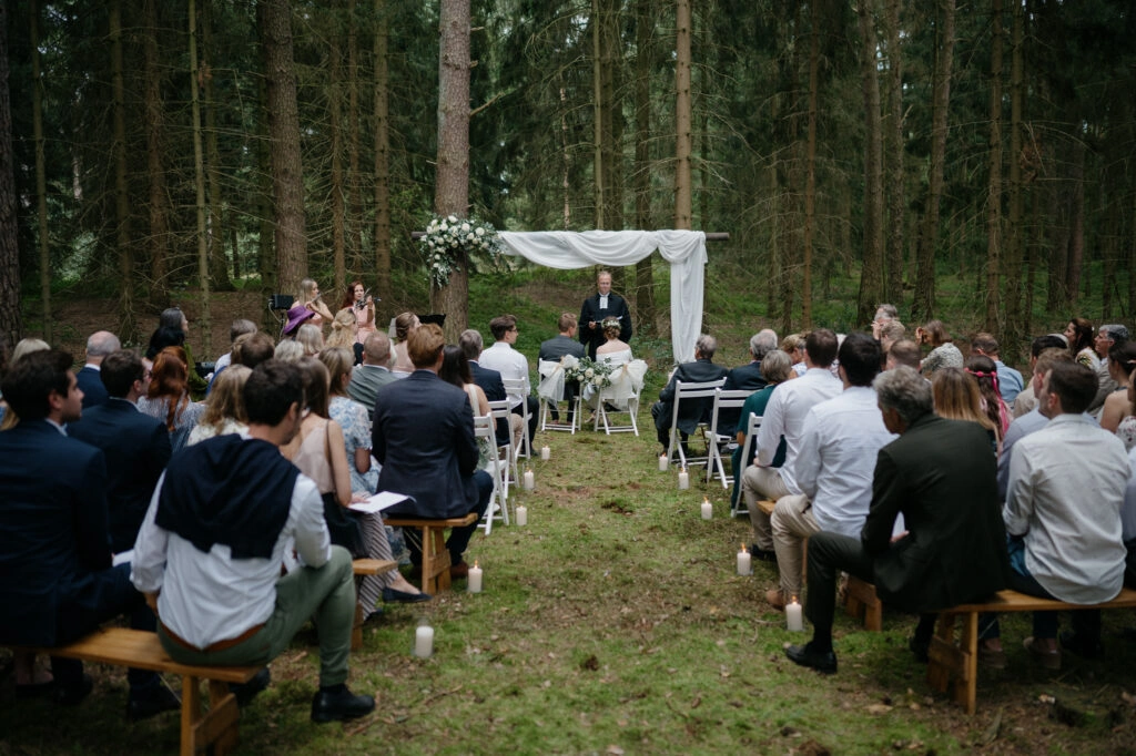 Freie Trauung vor einem weißen Bogen im Wald.