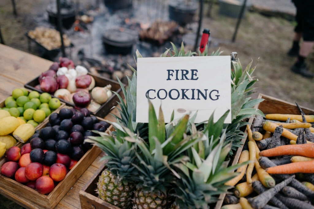 Gemüse und Obst neben einem Schild zum Kochen am Feuer.