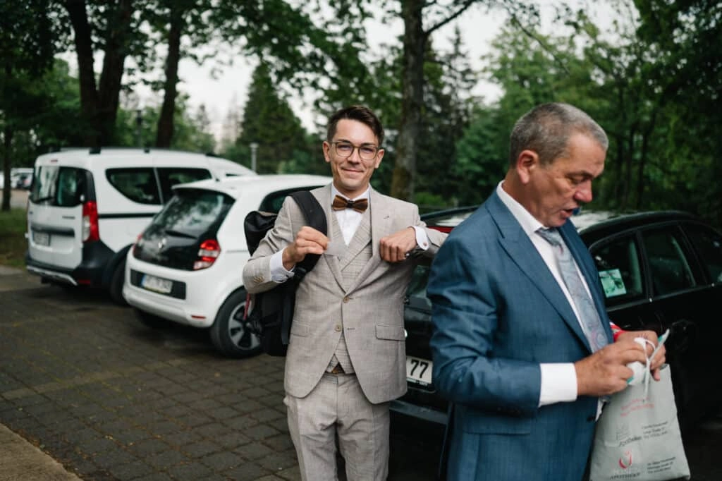 Bräutigam richtet seine Hosenträger neben einem Hochzeitsgast.