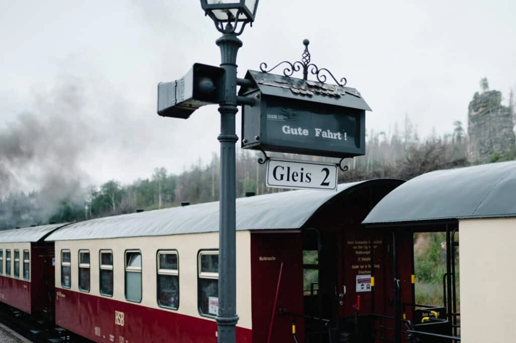 Bahnsteigschild und historische Wagen am Bahnhof.