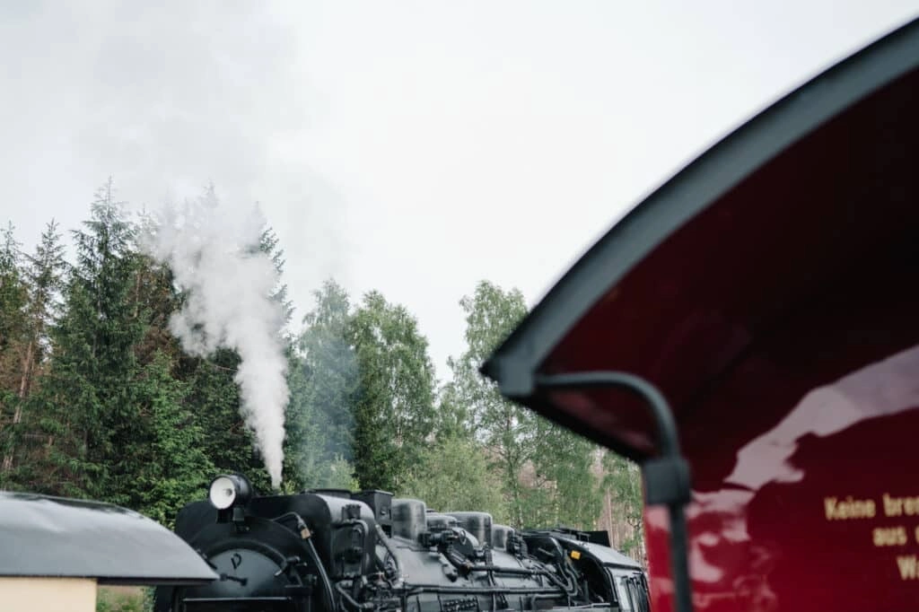 Dampflokomotive neben einem roten Personenwagen.
