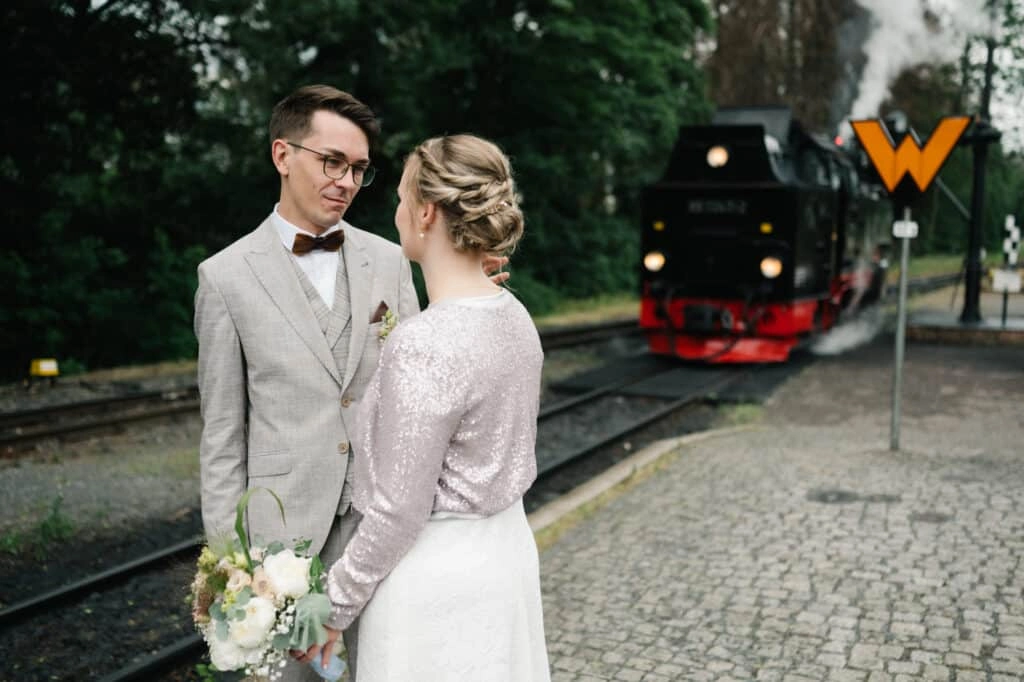 Brautpaar steht vor einer Dampflokomotive am Bahnhof.