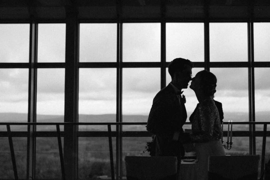 Brautpaar steht als Silhouette vor den Panoramafenstern.