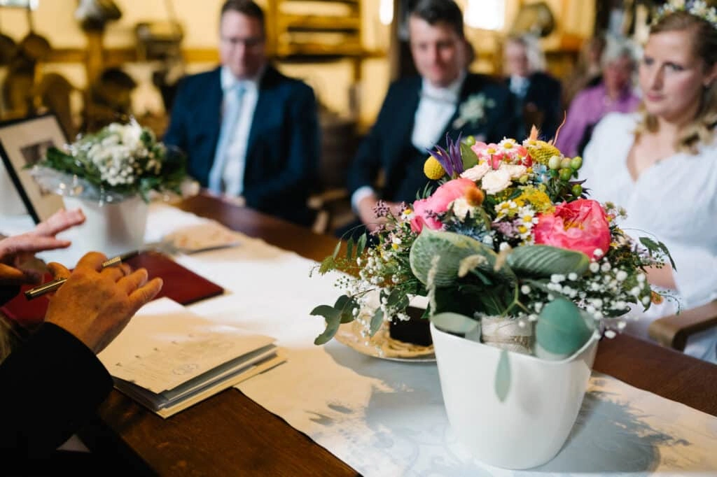 Brautpaar sitzt mit buntem Blumenstrauß am Trautisch.