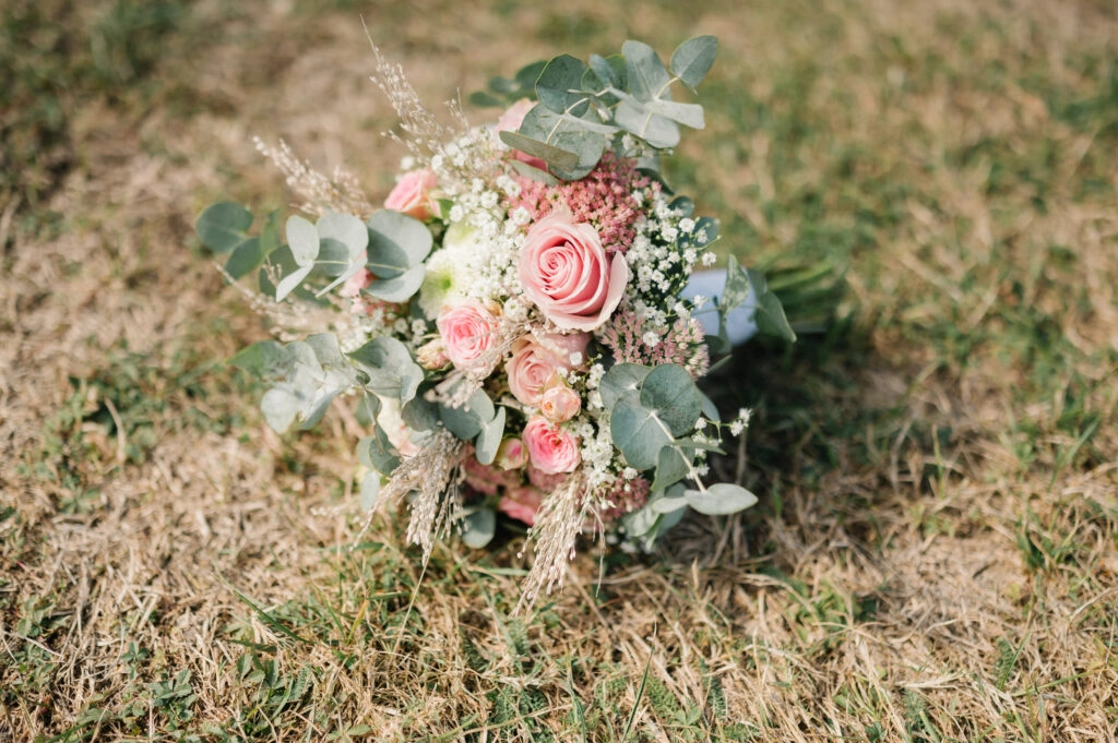 Rosa Brautstrauß mit Eukalyptus liegt im Gras.