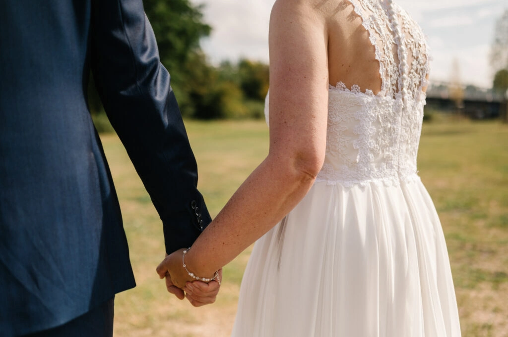 Detail der verschränkten Hände neben dem weißen Brautkleid.