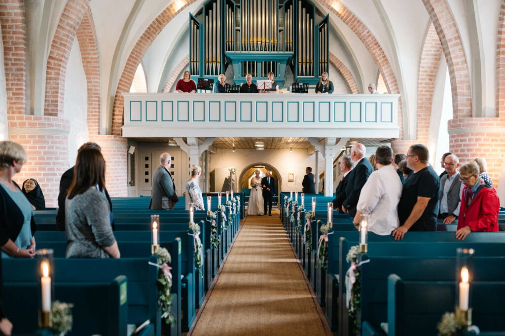Hochzeitsgäste stehen in den blauen Kirchenbänken.