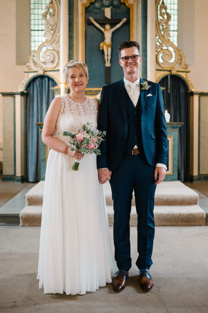 Brautpaar steht mit Blumenstrauß vor dem Altar.