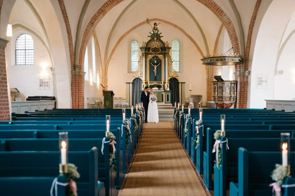 Blick durch den Mittelgang auf das Brautpaar vor dem Altar.