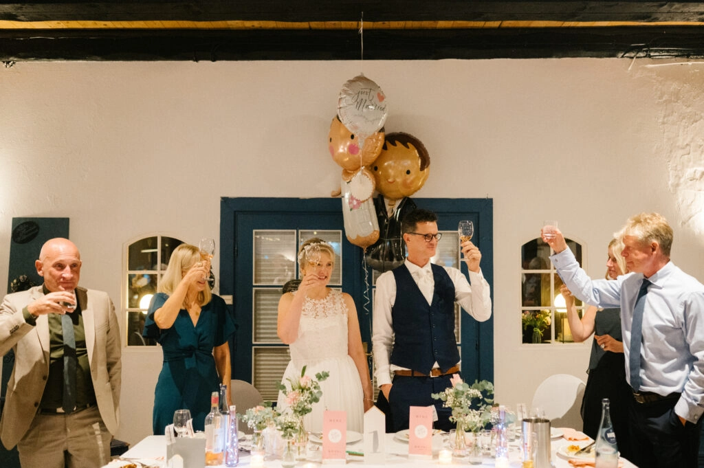 Brautpaar und Gäste stoßen an der Hochzeitstafel an.