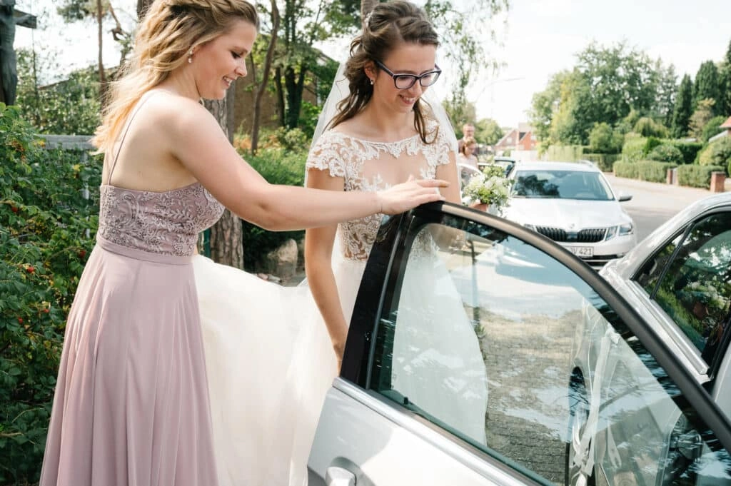 Eine Begleiterin hilft der Braut am Hochzeitsauto.