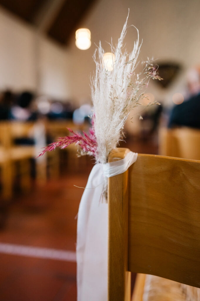 Trockenblumen und weißes Band schmücken eine Kirchenbank.