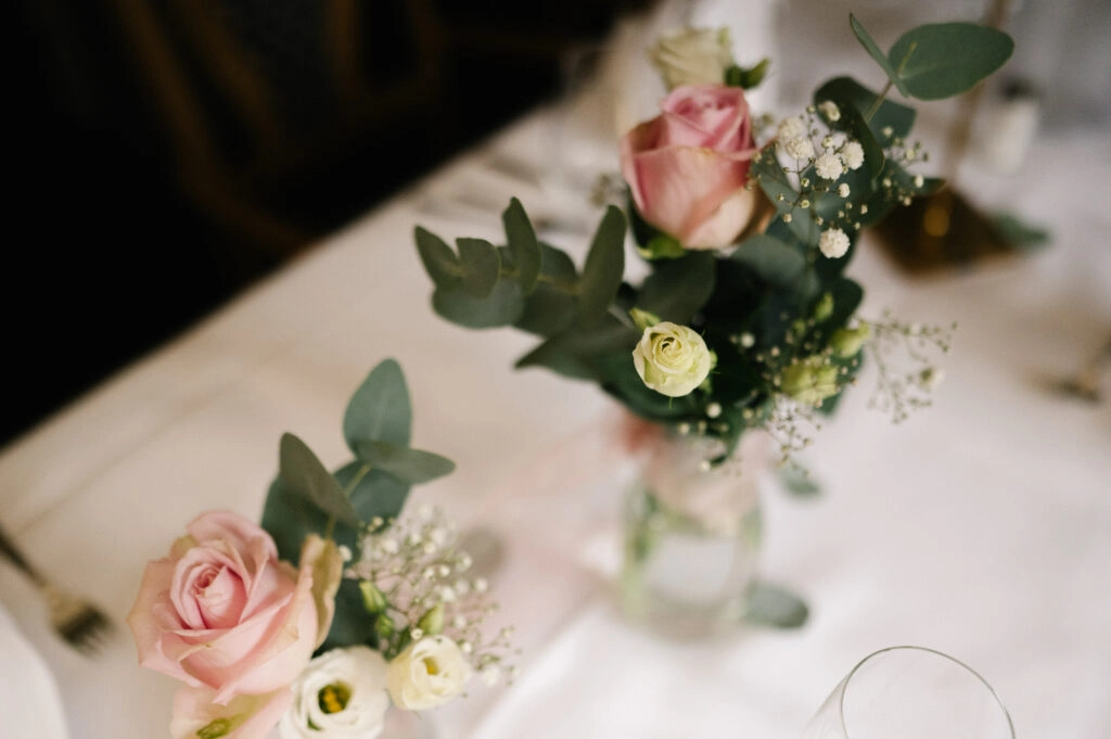Kleine Blumenvasen schmücken einen weißen Hochzeitstisch.