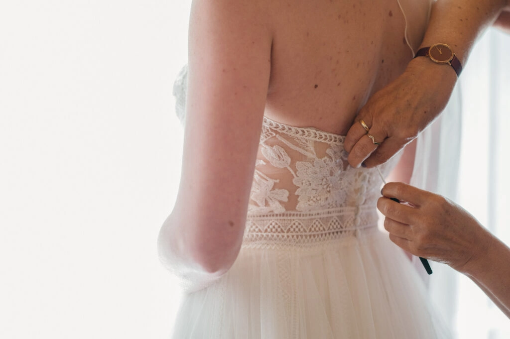 Helfende Hände schließen die Knöpfe am Brautkleid.