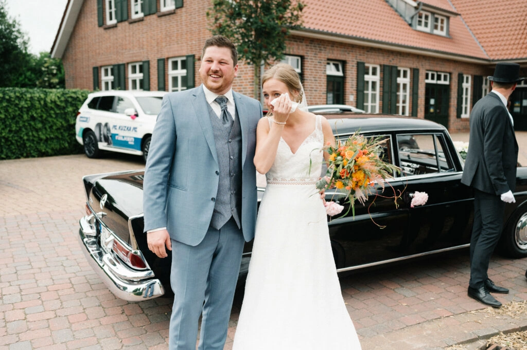 Brautpaar neben dem geschmückten Hochzeitsauto.