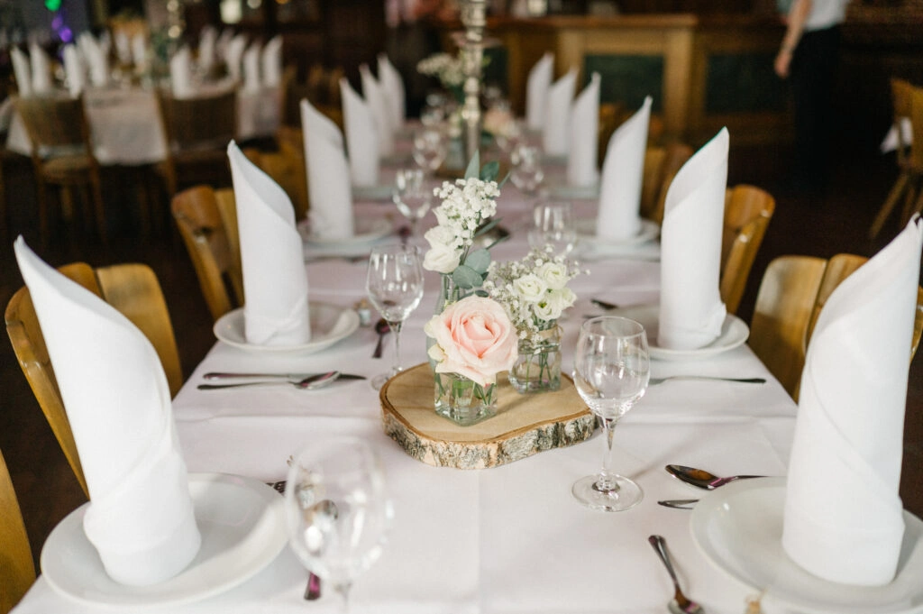 Gedeckter Hochzeitstisch mit Blumen und gefalteten Servietten.