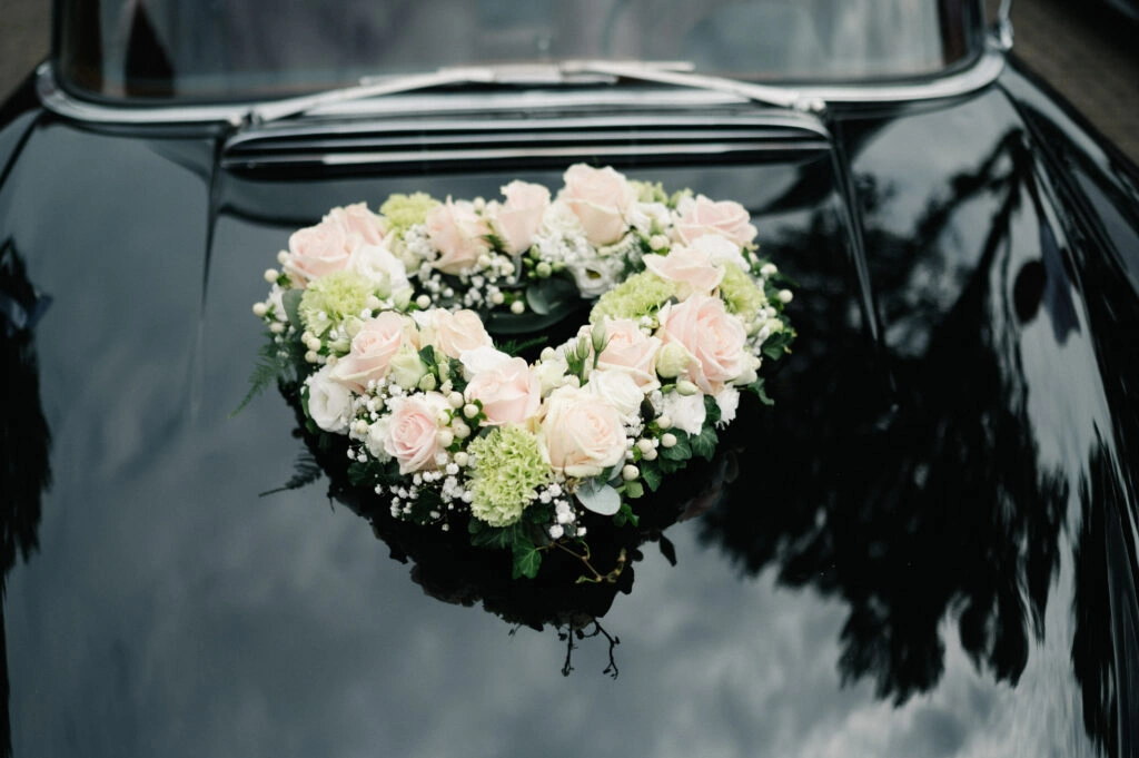 Blumenherz auf der schwarzen Motorhaube des Hochzeitsautos.