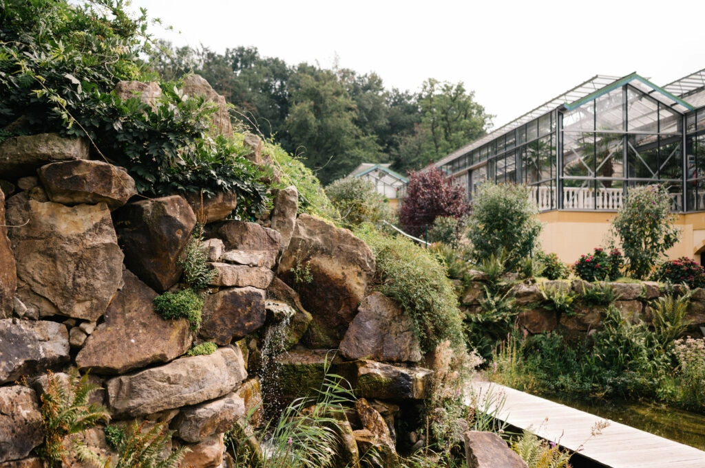 Steingarten mit Wasserlauf neben einem Gewächshaus.
