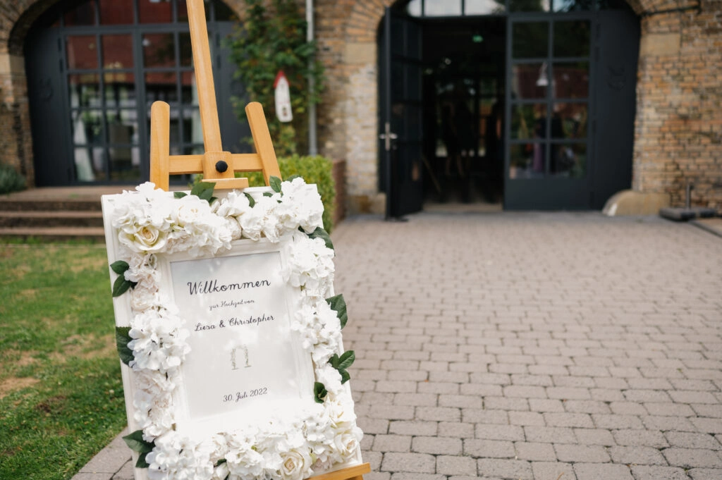 Blumengeschmücktes Hochzeitsschild auf einer Staffelei.