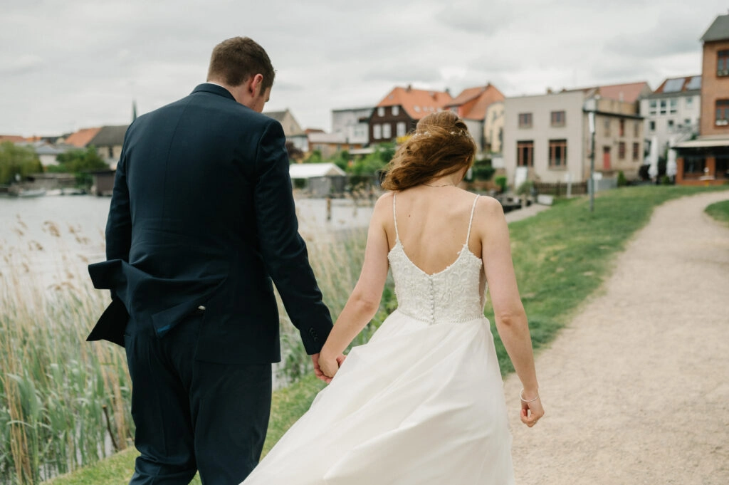 Brautpaar geht Hand in Hand am Ufer entlang.