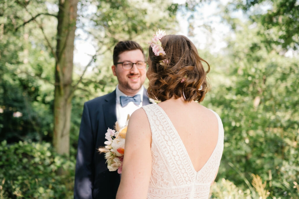 Braut mit Blumenschmuck im Haar vor dem Bräutigam.