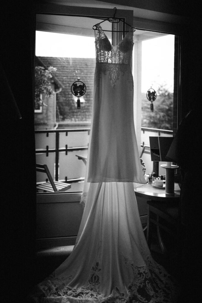 Brautkleid hängt vor einem Fenster, in Schwarz-Weiß.