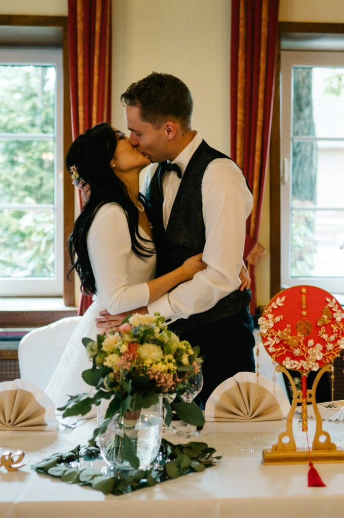 Brautpaar küsst sich an der Hochzeitstafel.