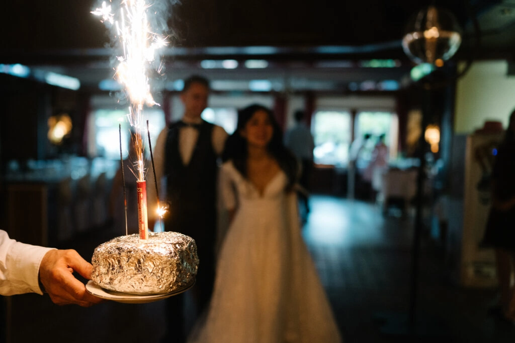 Kleine Torte mit brennender Wunderkerze vor dem Brautpaar.
