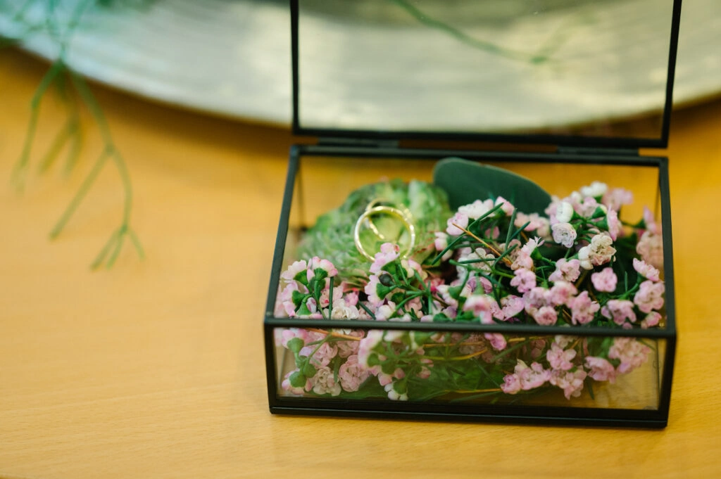 Eheringe in einer mit Blumen gefüllten Glasschatulle.