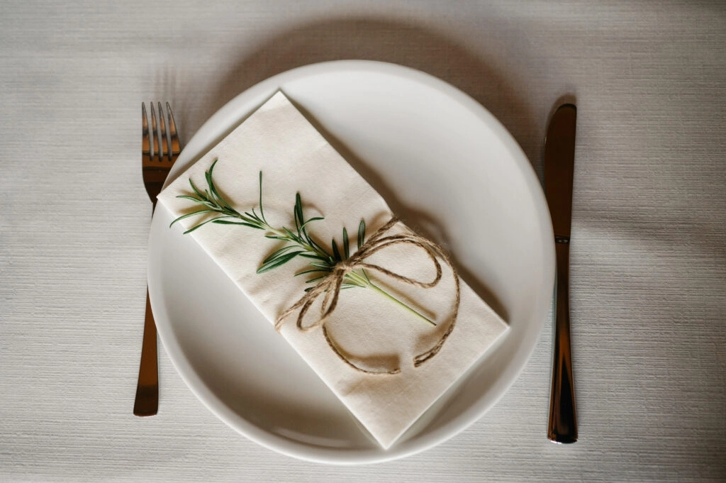 Gedeckter Platz mit gefalteter Serviette und Rosmarinzweig.