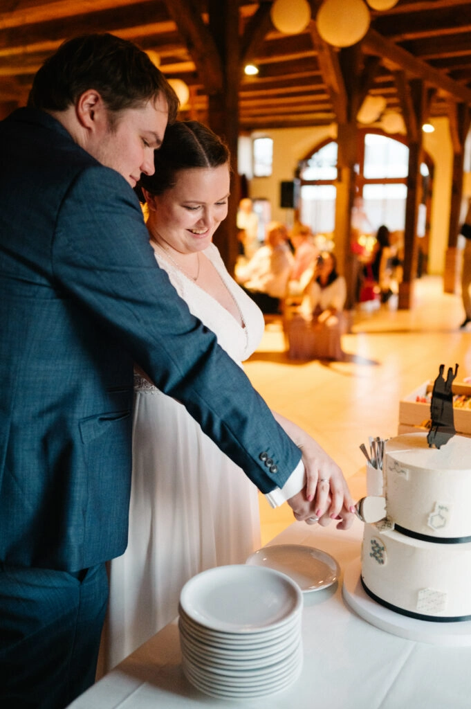 Brautpaar schneidet gemeinsam eine mehrstöckige Hochzeitstorte an.
