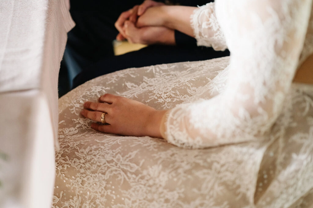 Nahaufnahme der Hände der Braut auf ihrem Spitzenkleid.