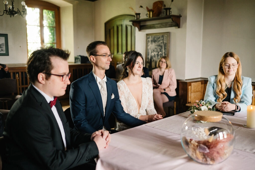 Brautpaar und Gäste sitzen während der Trauung am Tisch.