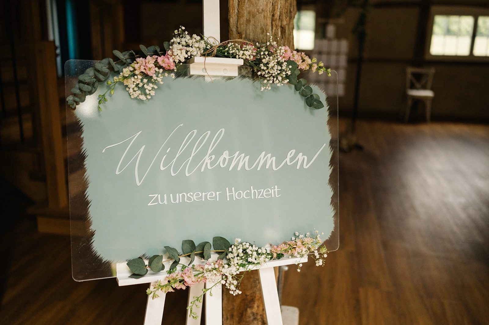 Grünes Willkommensschild mit Blumenschmuck.