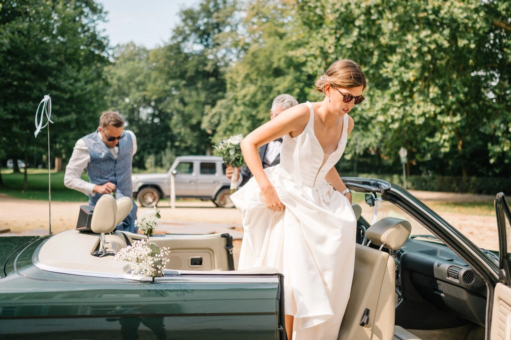 Braut steigt aus dem grünen Hochzeitscabrio.