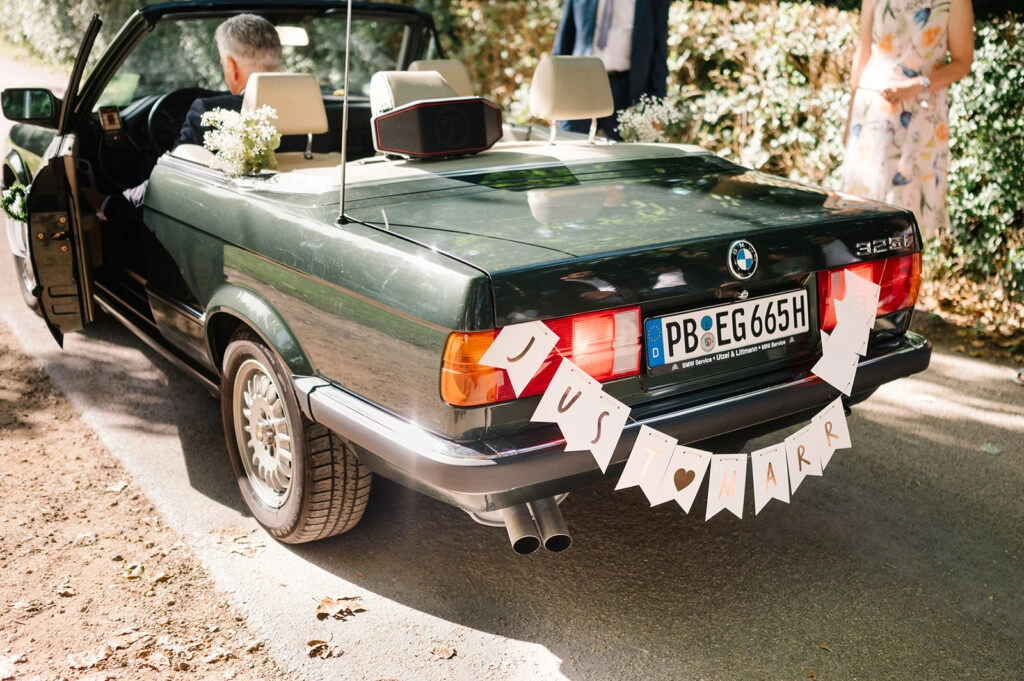 Grünes Hochzeitscabrio mit Girlande am Heck.