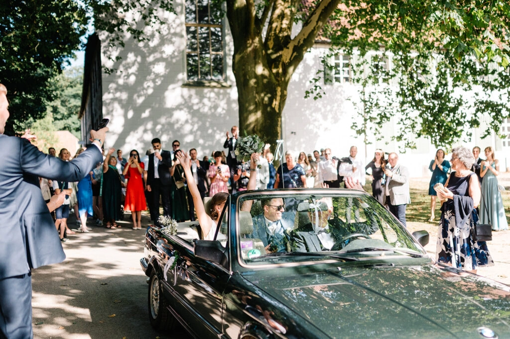 Gäste verabschieden das Brautpaar im Cabrio.