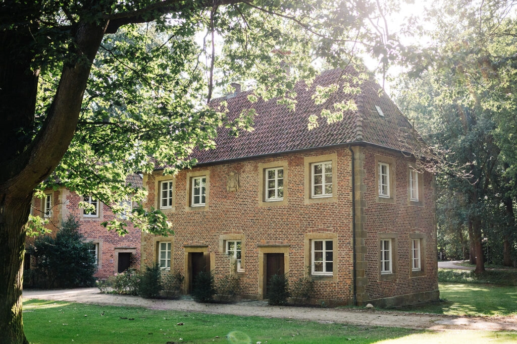 Historisches Gebäude mit rotem Dach unter Bäumen.