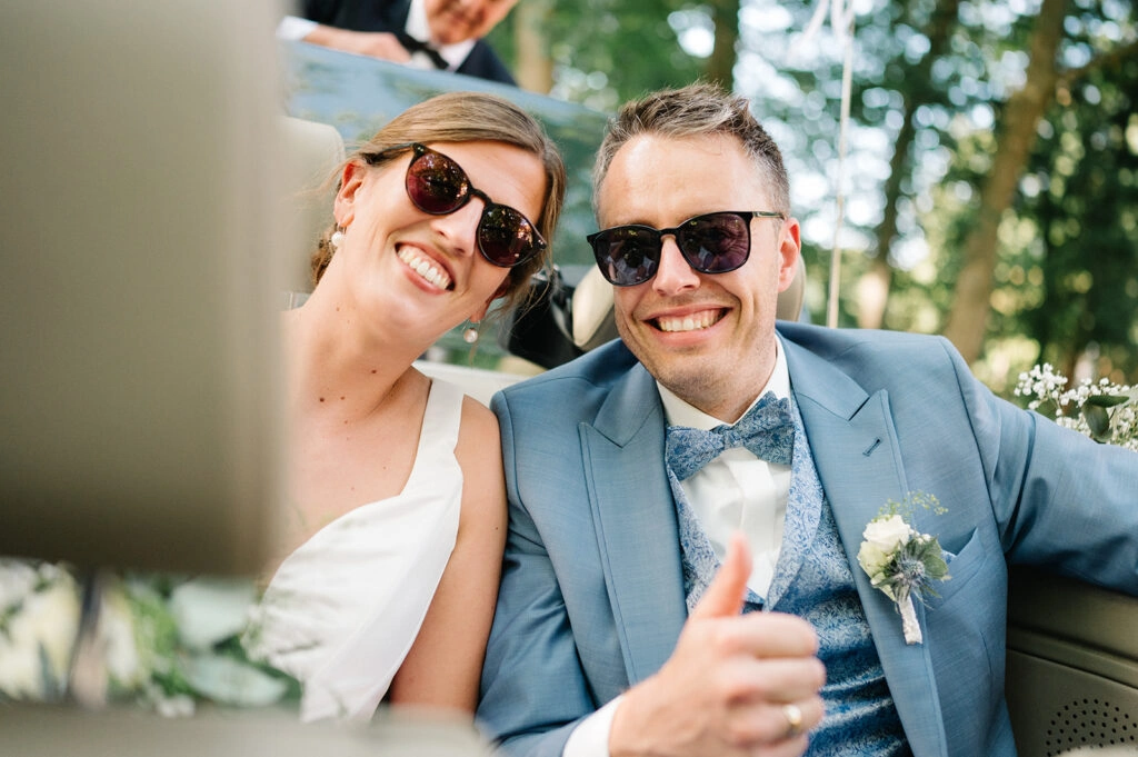 Brautpaar mit Sonnenbrillen im offenen Hochzeitsauto.