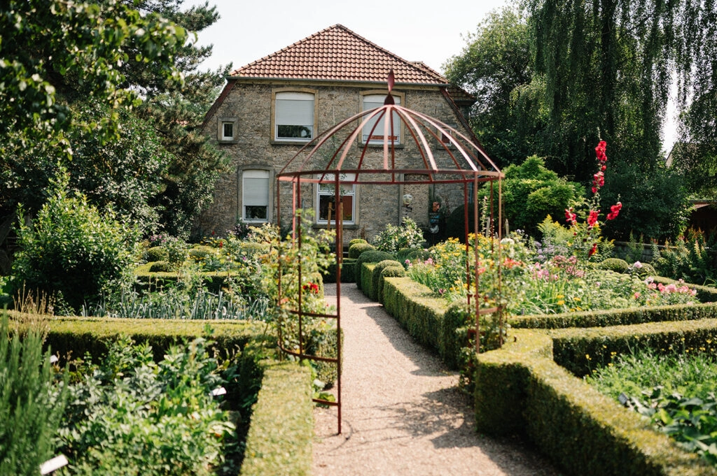 Garten mit Rosenbeeten und einem Rankpavillon.