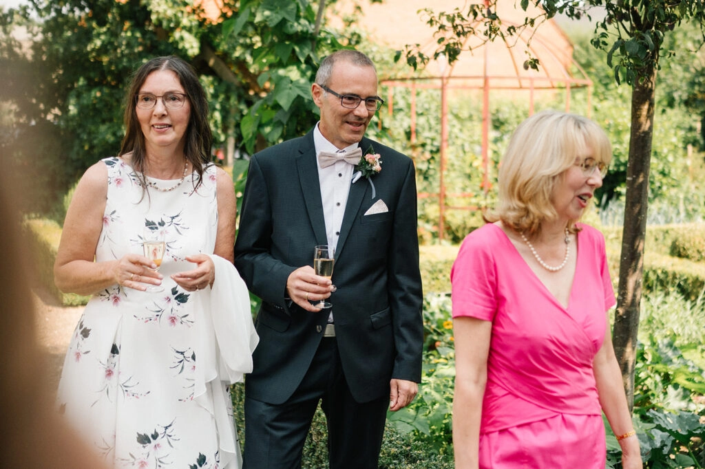 Brautpaar geht mit einem Gast durch den Garten.