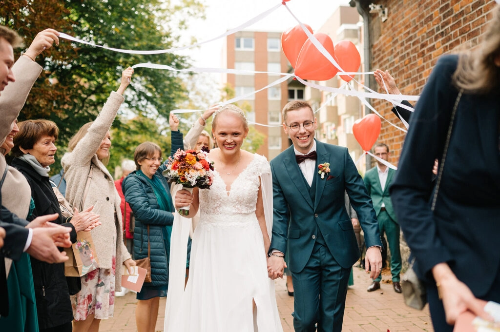 Brautpaar geht unter Bändern und Herzballons hindurch.