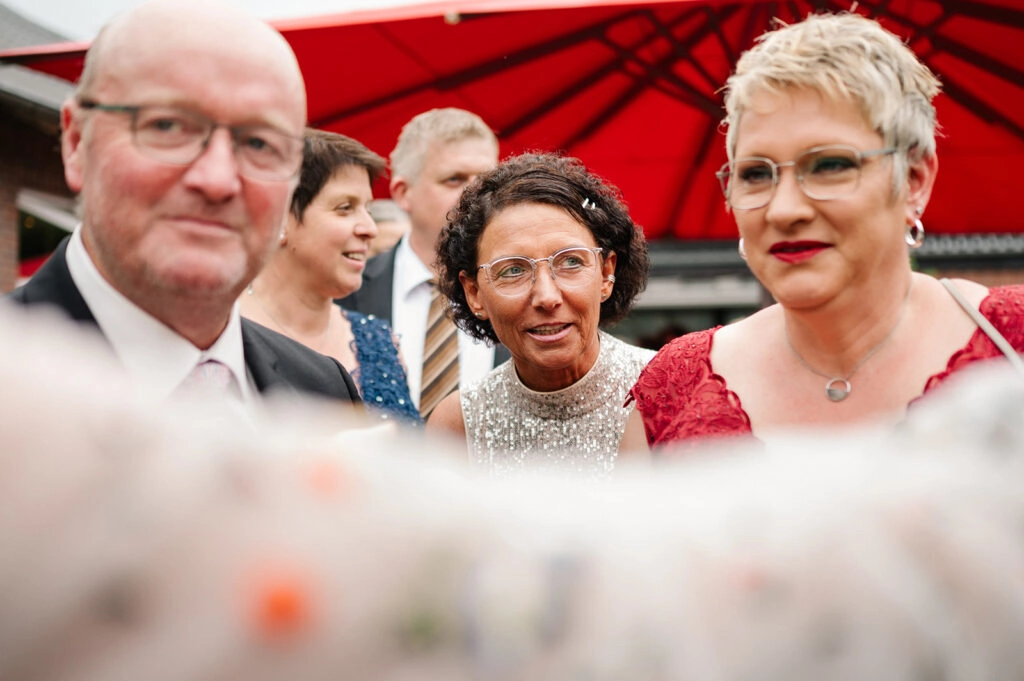 Hochzeitsgäste beim Empfang unter einem roten Schirm.