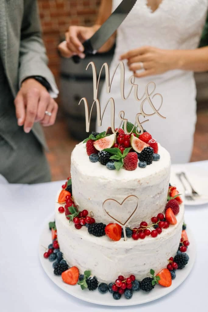 Brautpaar schneidet eine mit Beeren verzierte Hochzeitstorte an.