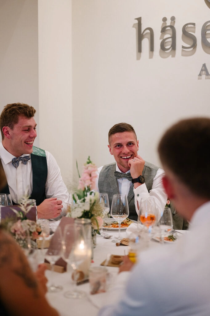 Gäste lachen gemeinsam an der Hochzeitstafel.