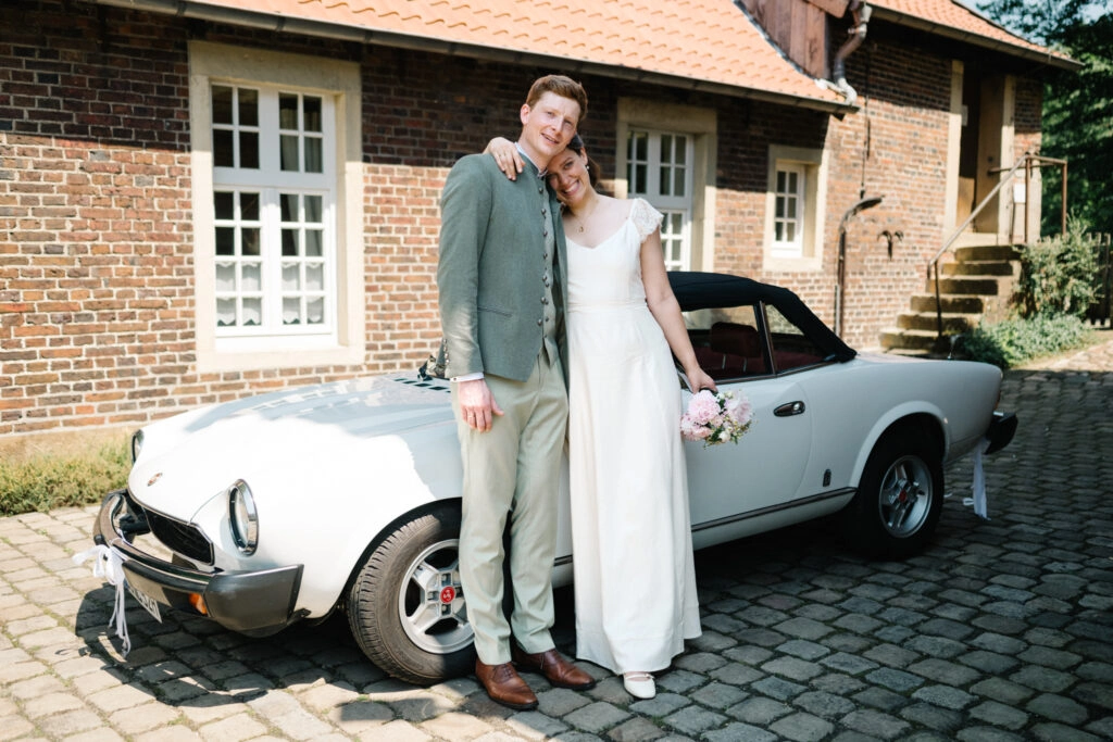 Brautpaar steht vor einem weißen Oldtimer.